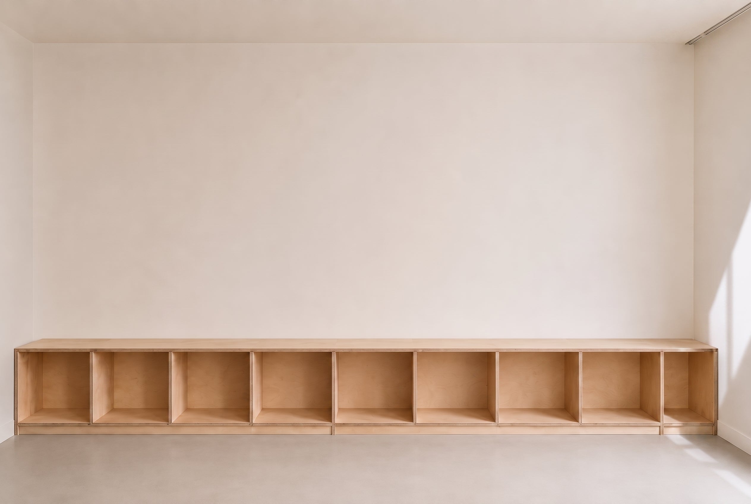 

Long open plywood cabinet fitted along a calm interior wall
